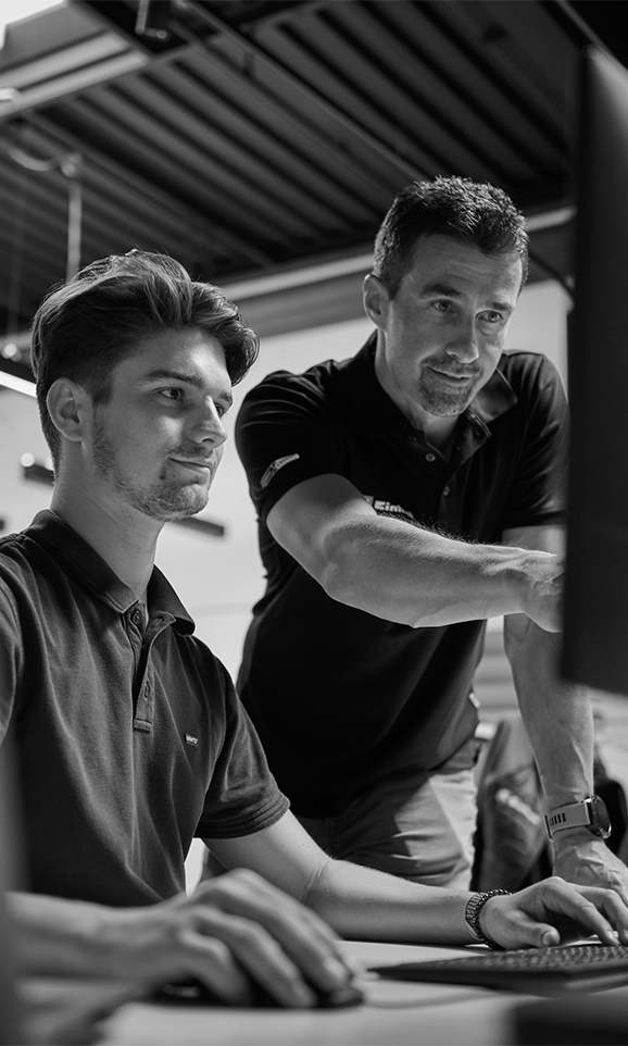 A young man and an older man working at a computer. The older man is pointing at the screen.