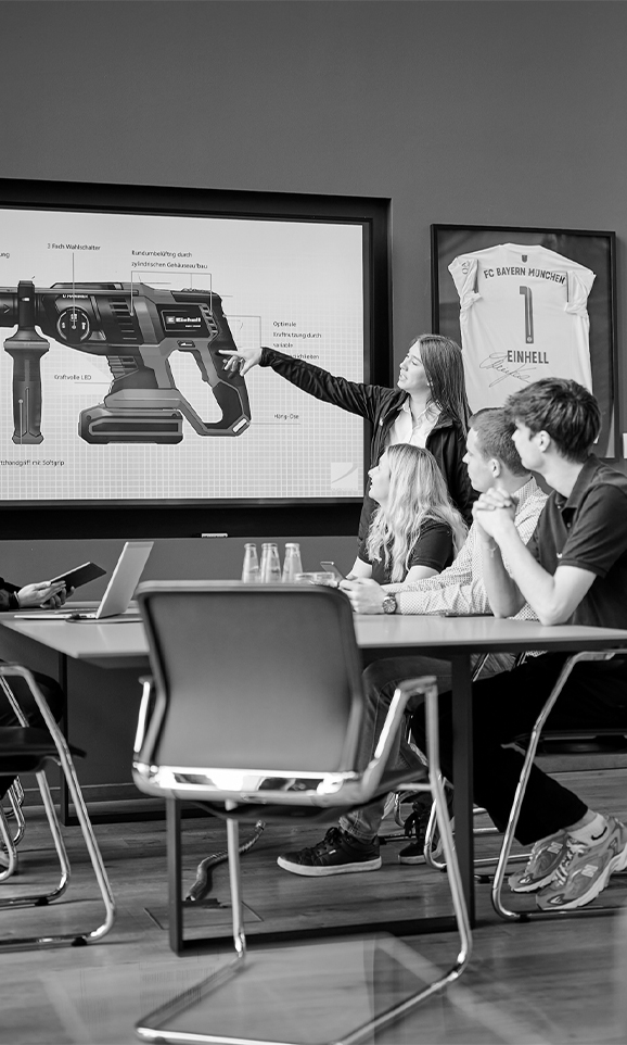 A woman is pointing at a screen with technical details of an Einhell rotary hammer. Four people are watching.