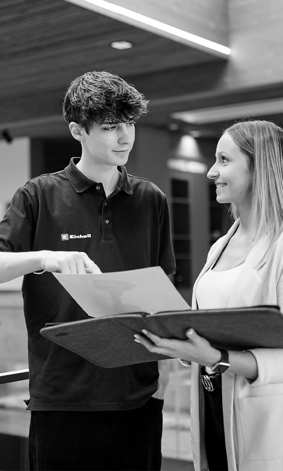 Two young Einhell employees in conversation. They are looking together at documents in an open folder.