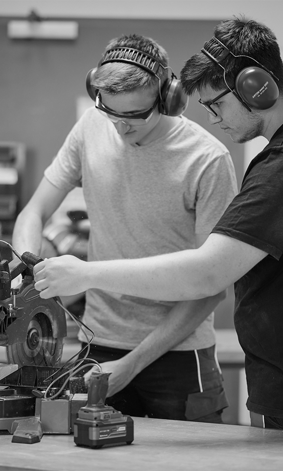 Two men wearing hearing protection work on a machine with an Einhell battery. They look focused.